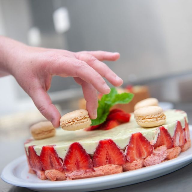 Mains déposant un macaron sur un fraisier