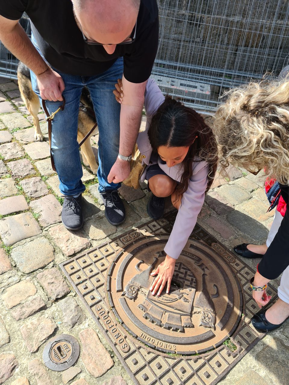 Haben Girma touchant une plaque d'égout historique à Saint-Malo, accompagnée par son traducteur Gordon