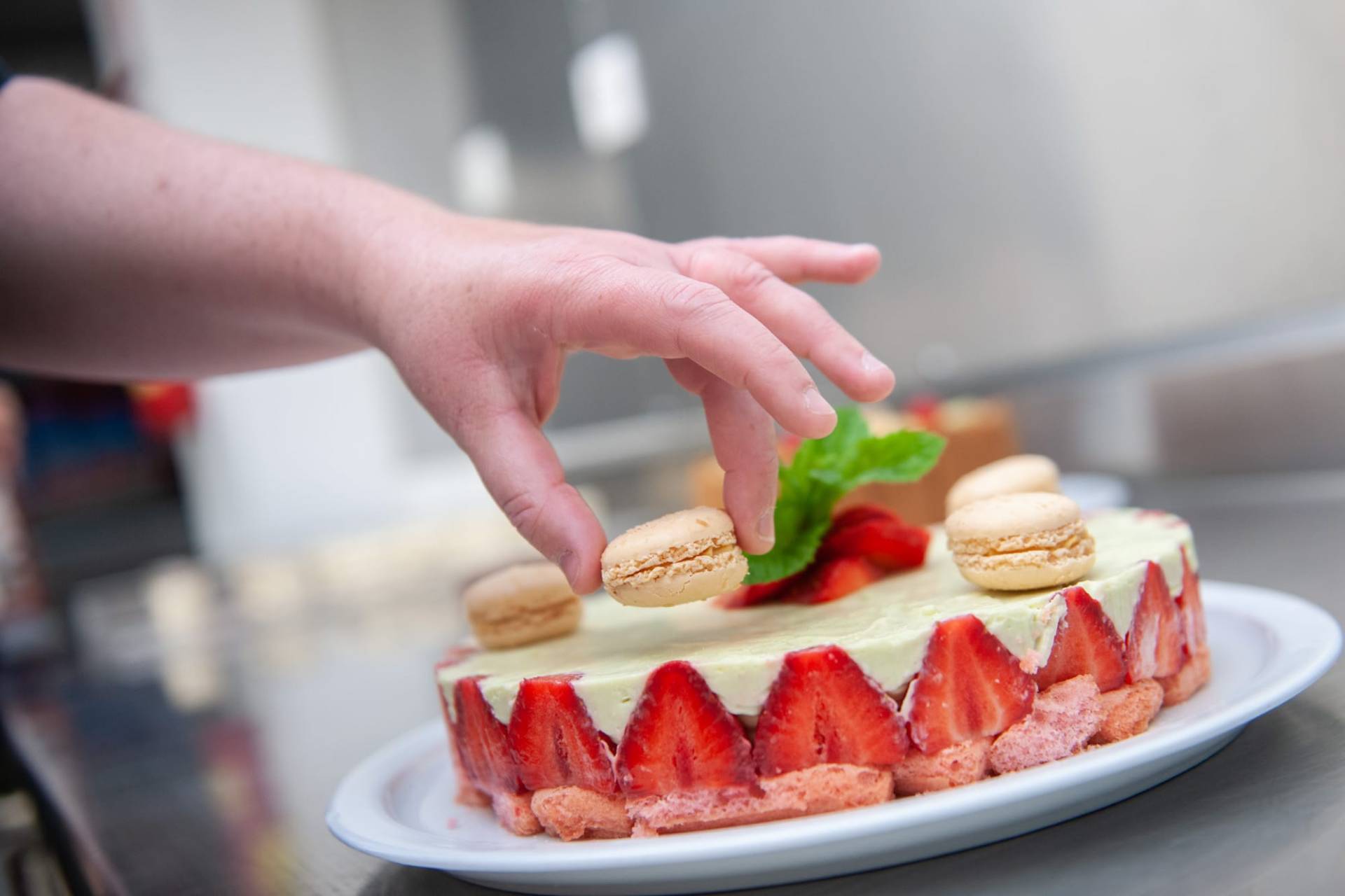 Main déposant un macaron sur un fraisier